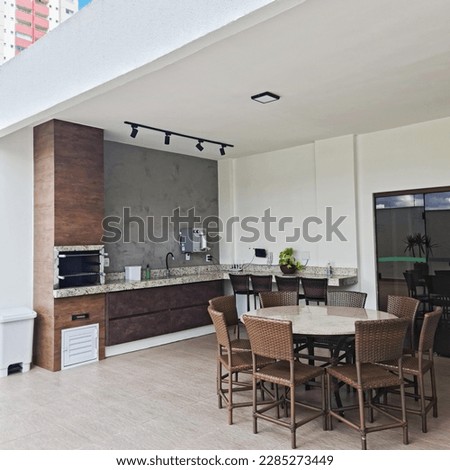Area with barbecue and grills for roasting meats, consisting of a cold water drinker, a granite table and woven hardware and chairs  Royalty-Free Stock Photo #2285273449