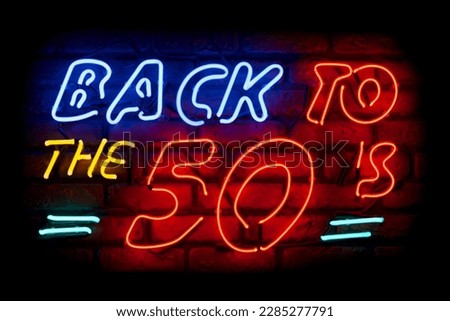 Neon light on a brick wall saying; Back to the 50's. Royalty-Free Stock Photo #2285277791