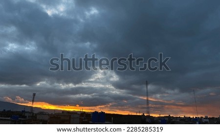 The heavy clouds in this picture are tinged with hues of orange and purple as the sun sets in the background. The dramatic contrast between the dark clouds and vibrant sky creates a breathtaking scene