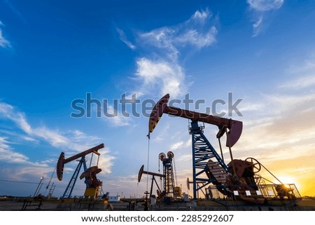 Oil field site, in the evening, oil pumps are running, The oil pump and the beautiful sunset reflected in the water, the silhouette of the beam pumping unit in the evening. Royalty-Free Stock Photo #2285292607