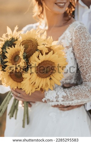 Wedding portrait. A red-haired bride in a white dress, holding a bouquet of sunflowers, on the background of a field. Beautiful curls. Sincere smile. Elegant dress. Yellow flowers