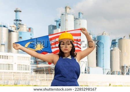 Sad asian female worker in hardhat with malaysian flag standing in front of factory