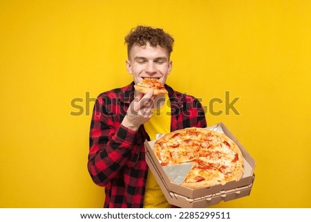 young happy guy eating pizza on yellow background, hungry student enjoying fast food