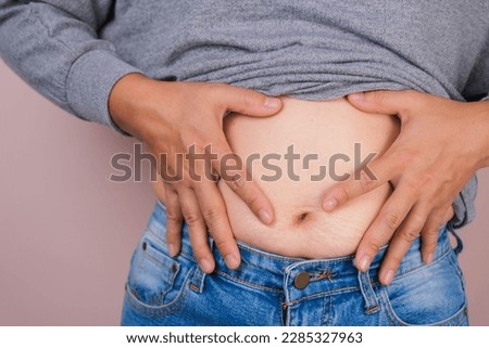 Fat woman hand holding excessive belly fat isolated on pink background. Overweight fatty belly of woman. Female diet and body health care concept