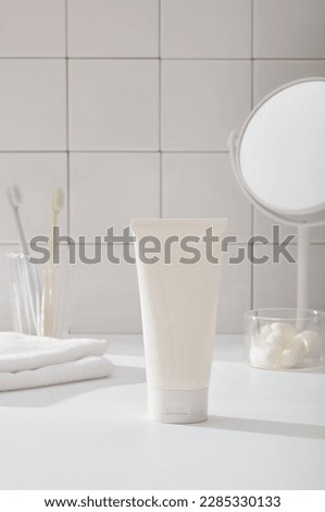 Bathroom concept with towel, toothbrushes, silkworm cocoons in transparent bowl, mirror on white tile wall background. In the middle is a plastic tube unlabeled mockup for cosmetic, cleanser product. Royalty-Free Stock Photo #2285330133