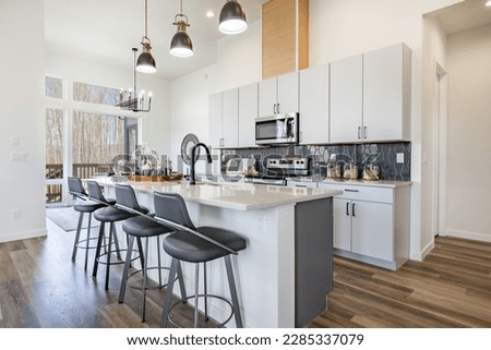 large working chefs kitchen with long white granite counter top hardwood floors grey cabinets stainless appliances large view windows dining table set for dinner Royalty-Free Stock Photo #2285337079