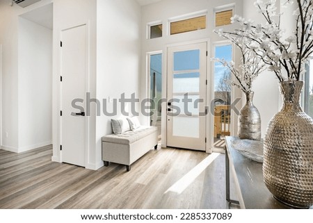 Bright white entry foyer with blue sky in glass door vase with flowers a storage bench and hardwood floors Royalty-Free Stock Photo #2285337089