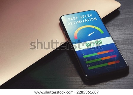 Boost mobile website performance with page speed optimization. High-value accelerometer on phone screen beside laptop on black wooden table for SEO digital marketing visuals Royalty-Free Stock Photo #2285361687