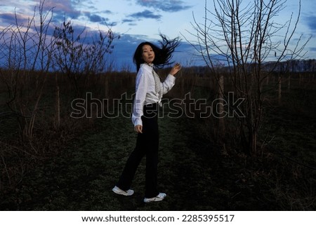 Dark atmospheric photo of a young asian girl walking by path at night in dark mysterious field.