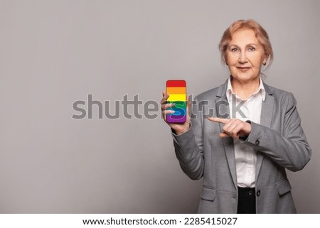 Happy senior mature woman showing modern smartphone with LGBT flag sceen. Stop discrimination, support concept