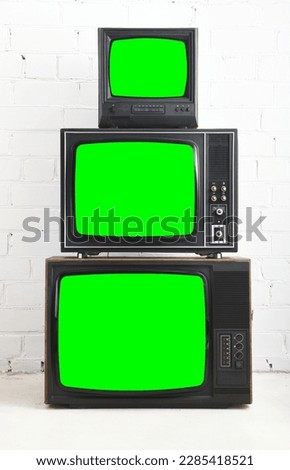 Three old televisions with a green screen against a white brick backdrop.