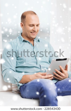 technology, people, winter and leisure concept - smiling man with tablet pc sitting on couch at home