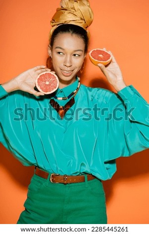 Overjoyed african american woman in summer clothes holding cut grapefruit on orange background