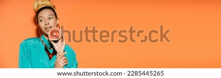 Well dressed african american woman holding fresh grapefruit on orange background, banner