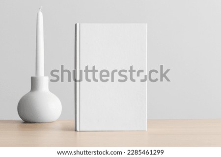 White book mockup with a candle on the wooden table.