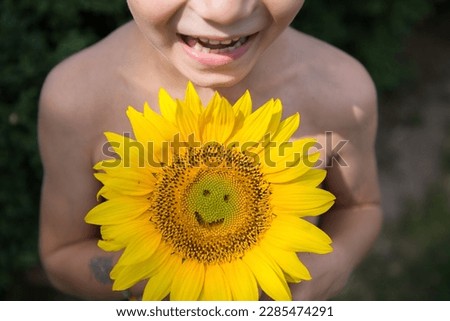 close-up of child's face and smile with milk teeth and yellow sunflower flower with smile carved into it. selective focus. positive atmosphere, happy childhood. mother's day gift. fun, joy. Hi summer