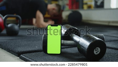 A video featuring a green screen smartphone and a man doing ab exercises in the background. This footage can be used to add customized text, images, or videos to the green screen area