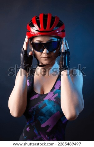 A young female cyclist wearing a safety helmet and glasses, dressed in a bib shorts poses against a black background in the studio. Royalty-Free Stock Photo #2285489497