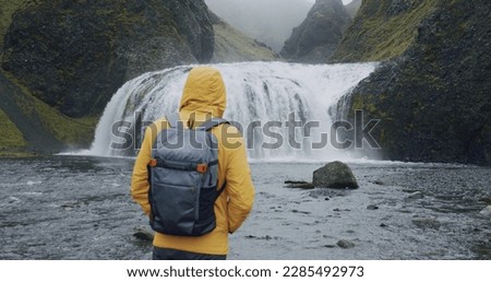 Iceland, man with backpack enjpying Stjornarfoss waterfall near Kirkjubaejarklaustur.