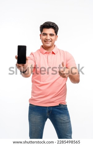 Young man standing in casual t shirt, showing smartphone screen and thumps up. Royalty-Free Stock Photo #2285498565