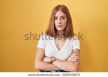 Young redhead woman standing over yellow background skeptic and nervous, disapproving expression on face with crossed arms. negative person.  Royalty-Free Stock Photo #2285518071