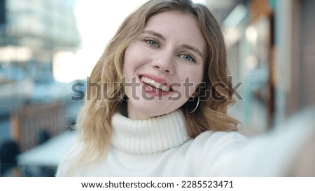 Young blonde woman smiling confident making selfie by camera at street