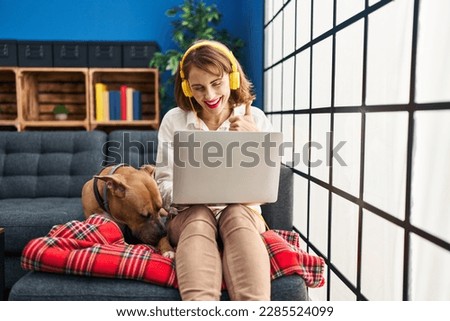 Young beautiful woman using laptop sitting on the sofa smiling happy and positive, thumb up doing excellent and approval sign 