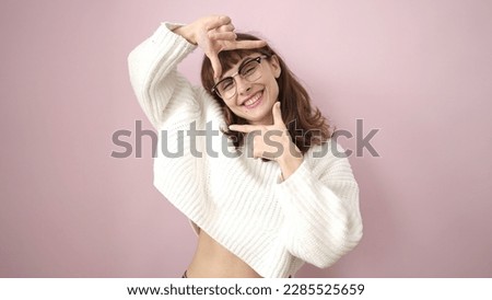 Young caucasian woman smiling doing frame shape with hands over isolated pink background