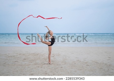 girl gymnast makes elements with a ribbon from rhythmic gymnastics, on the beach with a beautiful ribbon