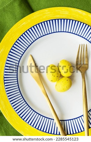 Easter serving concept. Close-up, vertical photo. Selective focus, noise. Festive table setting with bright napkins and yellow-blue plates with dishes and decorated eggs