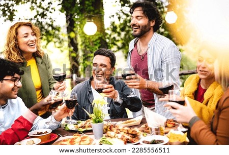 Happy men and women having fun drinking out at wine farm garden - Food and beverage life style concept on mixed age friends enjoying time together at home patio - Warm filter with bulb string lights Royalty-Free Stock Photo #2285556511