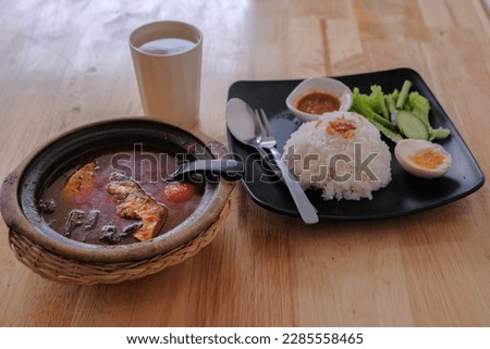 A picture of Ikan Kembung "asam pedas" with white rice on a wooden background. "Asam pedas" is sour soup made from tamarind, chilli and spices that is popular in Malaysia