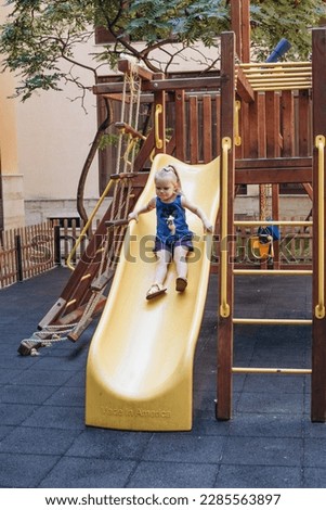a little girl plays on the playground and rides a slide