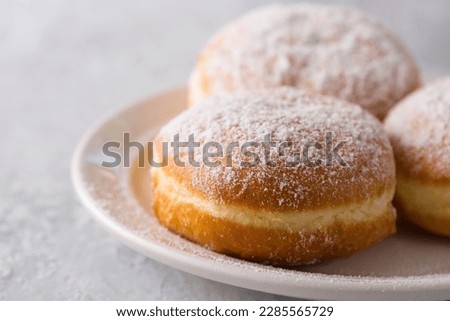 Ruddy delicious donuts berliners with filling sprinkled with powdered sugar on a white plate on a grey background