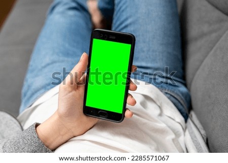 girl uses a smartphone with a green screen while sitting on the couch