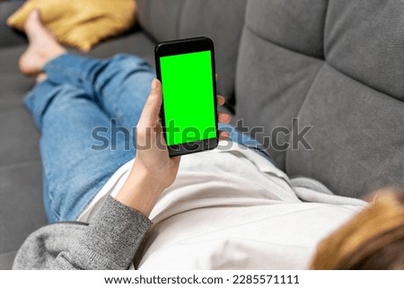  girl is lying on the couch , holding a smartphone with a green screen