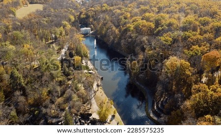 Beautiful panoramic autumn landscape park, many trees with yellow leaves, lake with fountain in center, architecture, big stones, paths walkways, people walking on sunny autumn day. aerial drone view