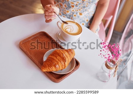 female hands with a cup of coffee and a croissant in a cafe. Close-up photo