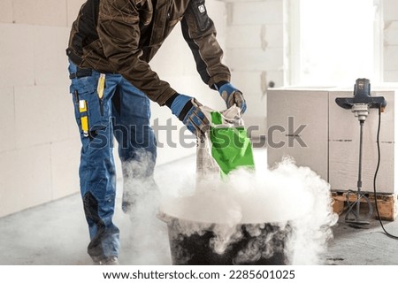 Construction work. Adding dry mortar mixture into clear water to make a mortar. Royalty-Free Stock Photo #2285601025