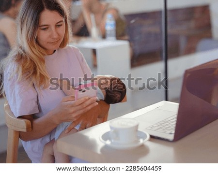 Diverse people portrait. Creative businesswoman balancing work and motherhood. Beautiful young mother working with laptop computer and breastfeeding, holding and nursing her newborn baby at cafe.