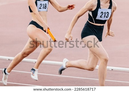 women running relay race in summer athletics championship, passing baton two female athletes Royalty-Free Stock Photo #2285618717