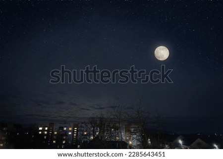 Full moon in dark star sky over town roofs.