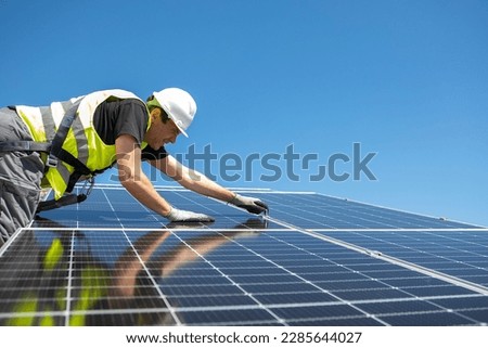 Man mounting modern solar batteries on house's roof. Environment friendly, green energy. Ecological. Using natural renewable energy. Wearing work uniform. High quality photo Royalty-Free Stock Photo #2285644027