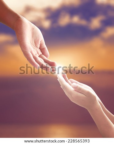 Hands of a man reaching to hand of GOD over blurred sunset background.