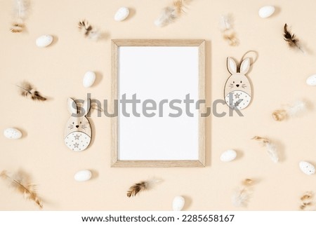 Easter trendy composition. Photo frame top view, feathers , easter eggs and bunny on beige background. Easter concept. Flat lay, top view, copy space