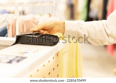 The buyer attached the credit card to the terminal to pay for the purchase. Hand close-up with bank card. A clothing store, a grocery mahazine, a mall.