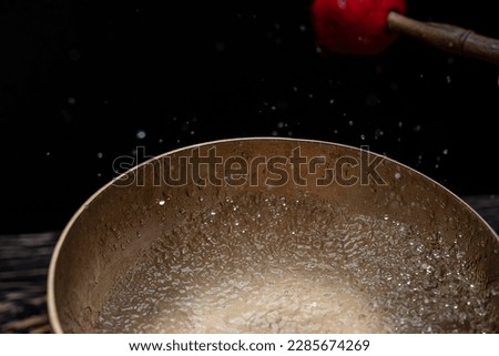 Drops of water fly into the air from hitting a Tibetan (singing) bowl. Cold boil. Tibetan bowl on a black background. High quality photo