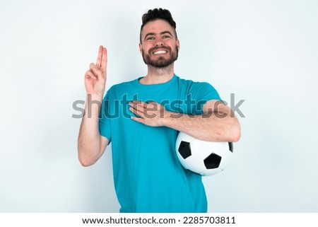young handsome man wearing blue T-shirt over white background smiling swearing with hand on chest and fingers up, making a loyalty promise oath.