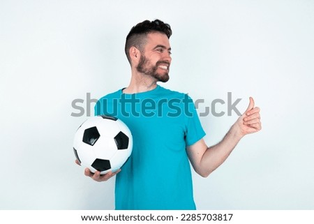 young handsome man wearing blue T-shirt over white background Looking proud, smiling doing thumbs up gesture to the side. Good job!