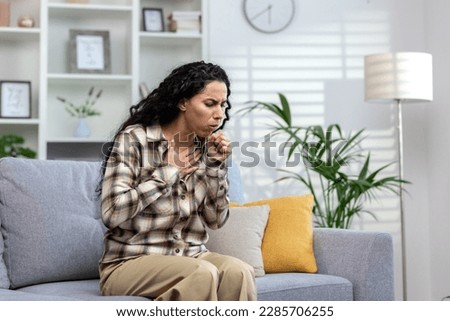 Woman having cold and sick coughing sitting on couch at home, hispanic woman in living room with cold and flu. Royalty-Free Stock Photo #2285706255